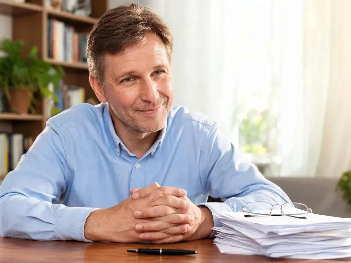 Ryszard Blaszka przy biurku w domowym gabinecie, z życzliwym, zamyślonym uśmiechem, w otoczeniu dokumentów i książek.