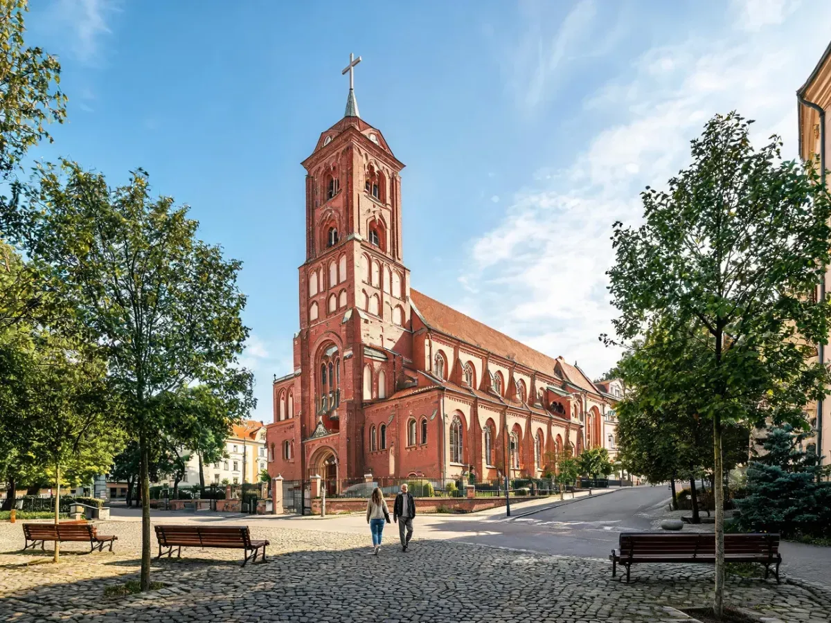 Kościół św. Antoniego Padewskiego w Poznaniu z wieżą, widok od spokojnego placu z ławkami i drzewami w słoneczny dzień.
