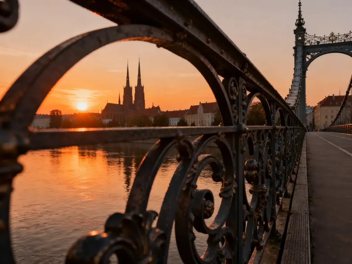 Zabytkowy most we Wrocławiu o zachodzie słońca z widokiem na rzekę Odrę i panoramę miasta w ciepłych barwach.