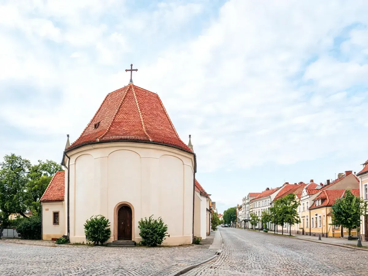Kościół parafii Ofiarowania Pańskiego w Poznaniu na spokojnej ulicy, jasna fasada, czerwony dach, krzyż na szczycie.