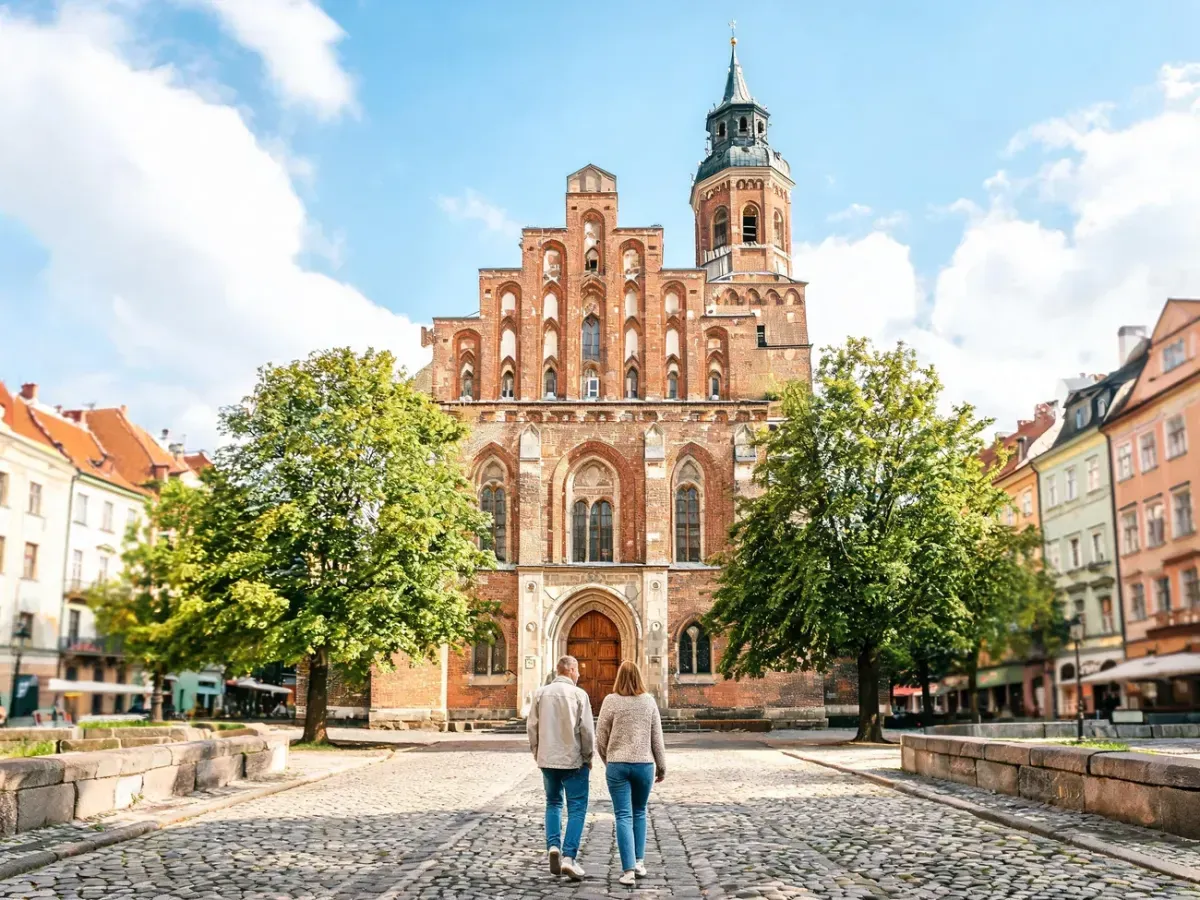 Ceglany kościół św. Karola Boromeusza w Poznaniu, widok z placu; wierni idą w stronę wejścia, słoneczny dzień.