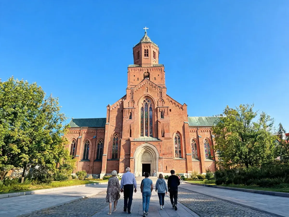 Wierni różnych pokoleń zmierzają do zabytkowego kościoła św. Michała Archanioła w Poznaniu w pogodny, słoneczny dzień.