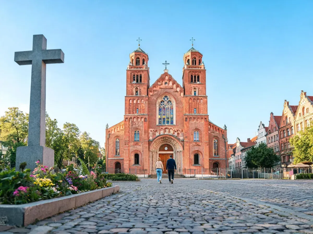 Zabytkowy kościół Świętego Krzyża w Poznaniu, wejście od frontu, wierni idący brukowaną ścieżką w słoneczny dzień