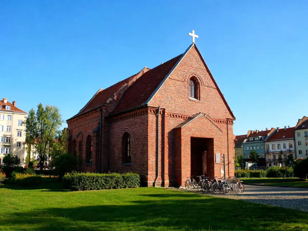 Zabytkowy kościół św. Jana Kantego w Poznaniu w słoneczny dzień, otoczony zielenią, ukazany jako spokojne miejsce modlitwy.